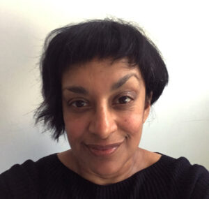 Tanuja's headshot. Tanuja is a black woman with short black hair. She is wearing a black round-neck top, looking straight ahead in front of a white, shadowed background. Her professional biography is adjacent.